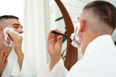 Reflection of a young man shaving in bathroom mirror close upの写真素材