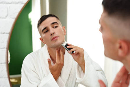 Reflection of a young man shaving in bathroom mirror close up