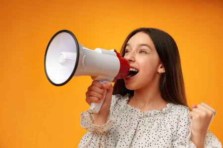 Teen girl making announcement with megaphone on yellow backgroundの写真素材