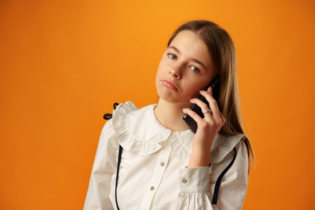 Teen girl over yellow wall talking on smartphone