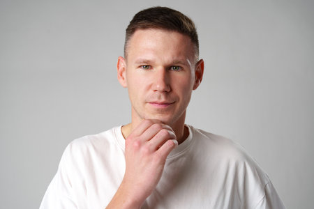 Thoughtful caucasian young male touching chin with hand thinking on gray backgroundの写真素材