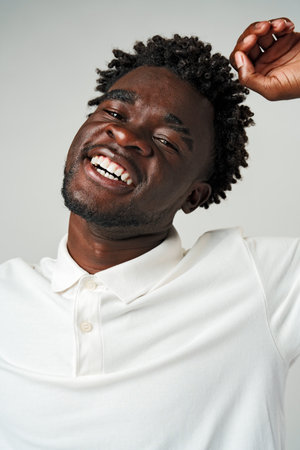Young African Man in White Shirt Celebrates With Joyful Fist Pump on Grey Backgroundの写真素材