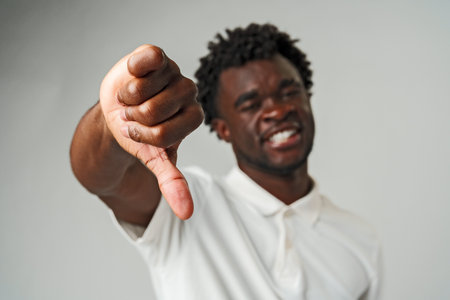 Young African Man Giving Thumbs Down Gesture Against a Neutral Background.