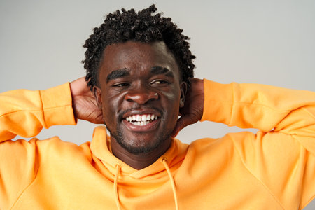 African Man in Yellow Hoodie Holding Head and Smilingの写真素材