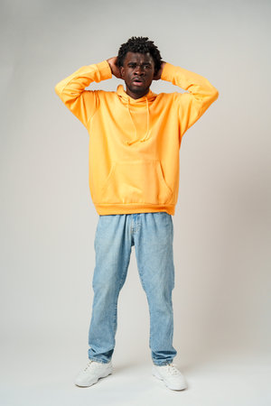 African Man in Yellow Hoodie Holding Head and Smilingの写真素材