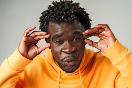 African Man in Yellow Hoodie Holding Head and Smiling