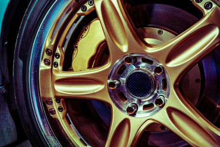 Close Up View of a Shiny Golden Alloy Wheel on a Blue Sports Carの写真素材