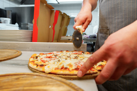 Chef Cutting Freshly Baked Pizza in a Commercial Kitchen Settingの写真素材