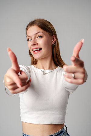 Smiling Young Woman With Braces Pointing Towards Camera in Studioの写真素材