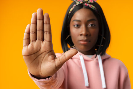 Young african woman over yellow background doing stop sign with palm of the hand