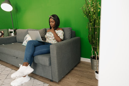 Young african woman working on laptop computer at home sitting on sofa.の写真素材