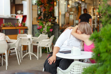Woman with disability sitting in a wheelchair in outdoor cafe with her young daughterの写真素材