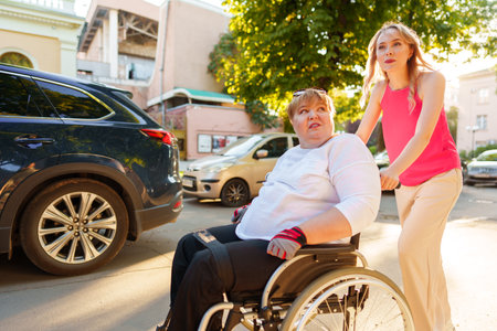 Young female caregiver pushing wheelchair with female person with disability across city streetの写真素材