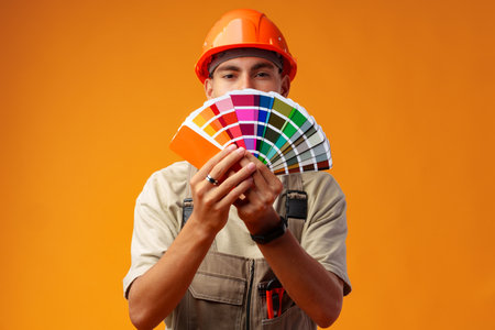 Handsome young worker in uniform holding paint samples palette on yellow backgroundの写真素材