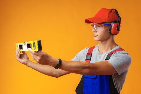Young male handyman holding construction spirit level on yellow backgroundの写真素材