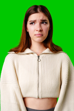 Young Woman Expressing Skepticism Standing Against Green Background in Casual Outfitの写真素材