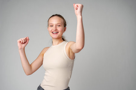 Young Woman in Casual Attire Smiling and Making a Fist Pump Gesture on a Plain Backgroundの写真素材