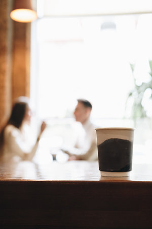 Two People Engage in Conversation Behind Coffee Cup on Wooden Tableの写真素材