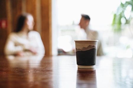 Two People Engage in Conversation Behind Coffee Cup on Wooden Tableの写真素材