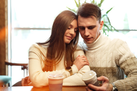 Smiling Couple Enjoying Warm Beverages at a Cozy Cafe on a Sunny Afternoonの写真素材