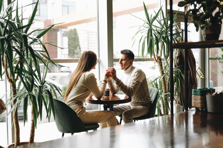 Couple Holding Hands Across Table in Cozy Cafe During a Daytime Dateの写真素材