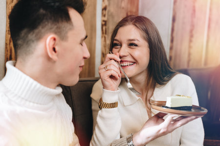 Young Man in White Sweater Enjoying Cheesecake With Friend at Cozy Cafeの写真素材