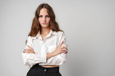 A woman is standing wearing a white shirt and black pants. She has a confident stance and is looking...