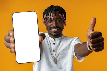 Excited young african man holding smartphone with white blank screen in hand on yellow studio backgroundの写真素材