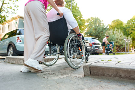 Young female caregiver pushing wheelchair with female person with disability across city streetの写真素材