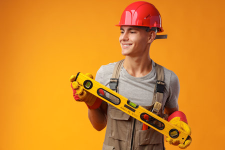 Young male handyman holding construction spirit level on yellow background