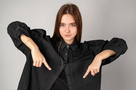 Young Woman in Black Shirt Pointing Downwards With Both Hands in Studioの写真素材