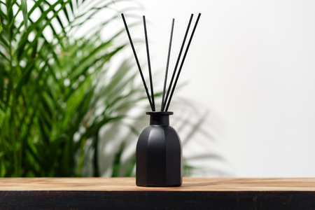 Black Reed Diffuser Bottle on Wooden Tabletop With Green Plantの写真素材