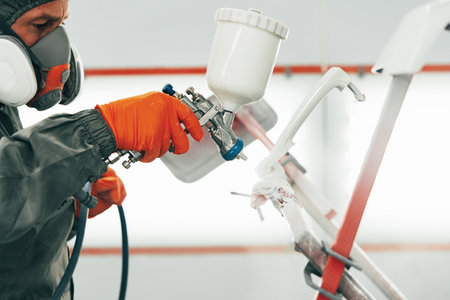 Male painter in respiratory mask and protective suit painting car with spray gun in car service