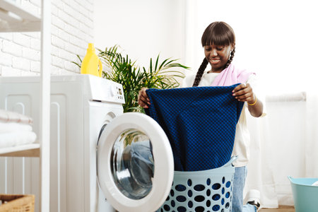 African Woman Folding Laundry After Washing Clothes in Modern Laundry Roomの写真素材