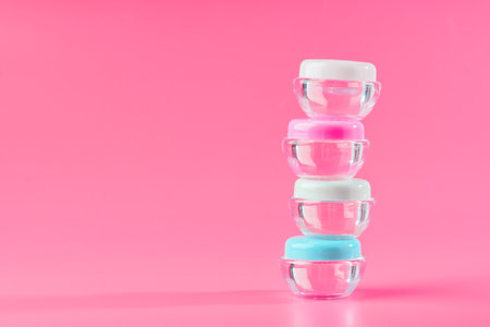 Stacked Clear Plastic Containers With Colored Lids on Pink Backgroundの写真素材
