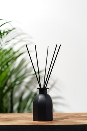 Black Reed Diffuser Bottle on Wooden Tabletop With Green Plantの写真素材