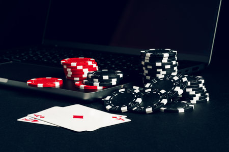 Red And Black Casino Chips On A Table With A Laptop And Playing Cardsの写真素材