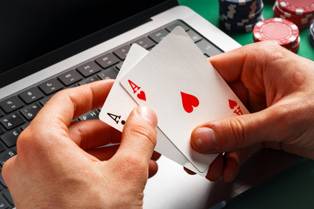 Person Playing Online Poker With Laptop and Cards
