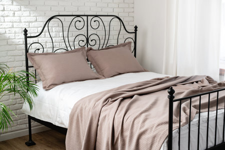 Black Metal Bed Frame With White and Beige Bedding in a Modern Bedroomの写真素材