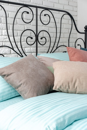 White Brick Wall Bedroom With Blue And Beige Pillows On A Bed With Black Metal Headboard