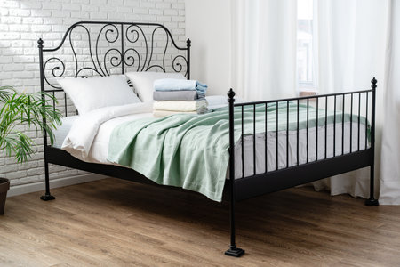 Black Metal Bed Frame With White Brick Wall And Green Blanketの写真素材