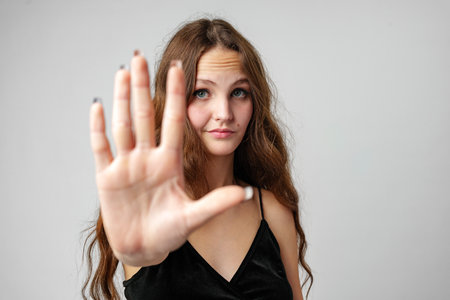 Young Woman With Long Brown Hair Holds Up Hand in Stop Gesture Against White Backgroundの写真素材