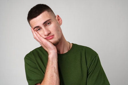Young Man With Short Hair Wearing a Green T-Shirt Posing With Hand on Chinの写真素材