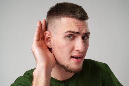 Young Man Holding Hand To Ear Listening Carefullyの写真素材
