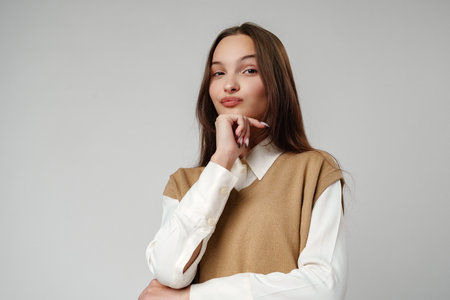 Young Woman Wearing a Brown V-Neck Sweater Vest Over a White Shirt and Beige Pantsの写真素材