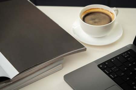 A Stack of Magazines, a Cup of Coffee, and a Laptop on a White Table