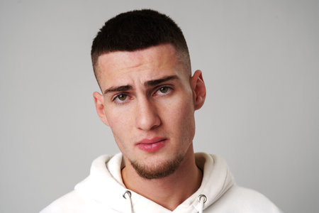 Sad Young Man Looking at Camera against gray backgroundの写真素材