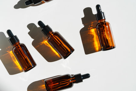 Arranged Amber Glass Bottles With Droppers on White Surface Accentuated by Shadows in Bright Lightの写真素材