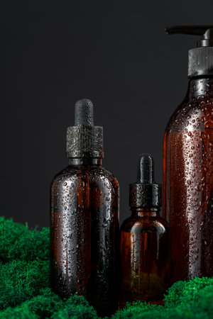 Dark glass bottles arranged on green moss against a black backgroundの写真素材
