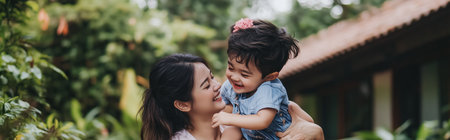 A joyful mother lifts her laughing child in a lush garden setting during a sunny afternoonの素材